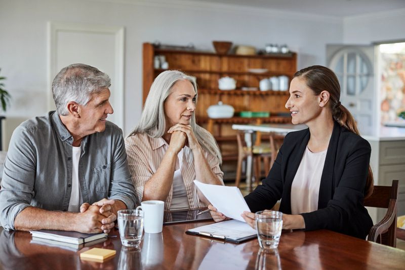 Mature man and woman listening to financial advisor. Female insurance agent is explaining contract to couple. They are at home.