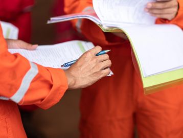 Workers in orange uniforms reviewing documents and taking notes.