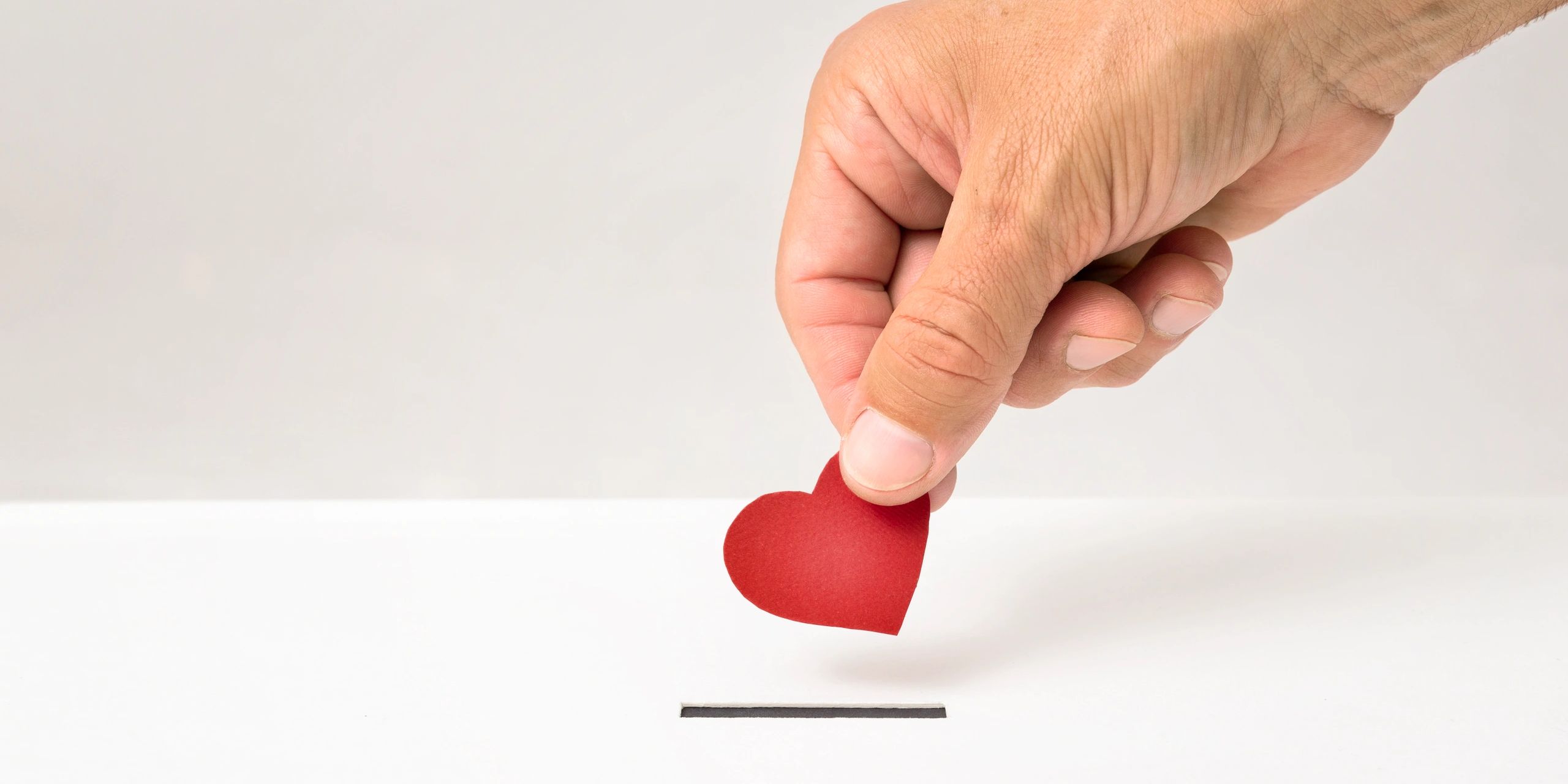 Hand placing a red paper heart into a slot, symbolizing love or charity.