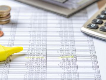 Financial spreadsheet with highlighted figures, a calculator, and coins.