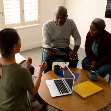Three adults having a discussion around a table with a laptop and notebooks.