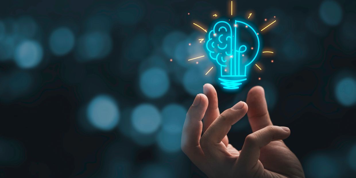Hand holding a glowing lightbulb with brain and circuit design.