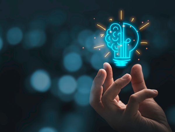 Hand holding a glowing neon light bulb with a brain inside, symbolizing creativity.