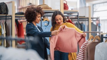 Two women shopping for clothes, examining a pink sweater.