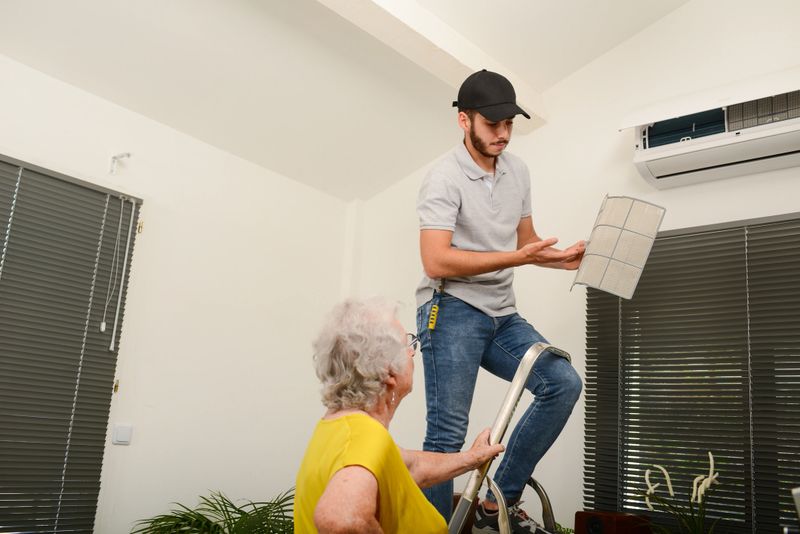 handsome young man electrician cleaning air filter on an indoor unit of air conditioning system in client house with senior woman