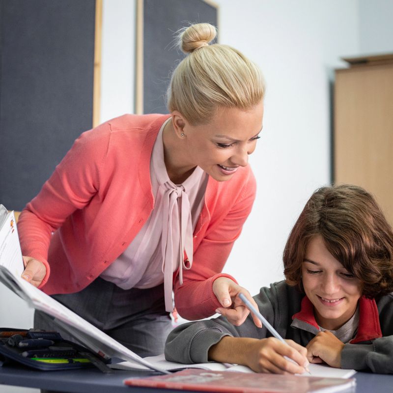 School teacher helping young male student with lecture in class