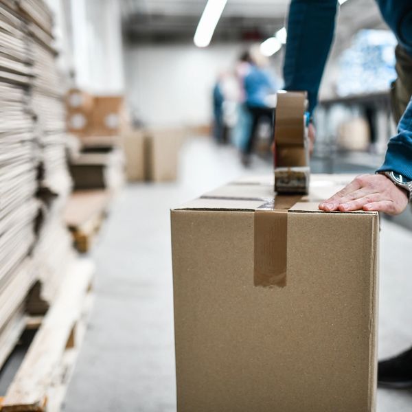 Person sealing a cardboard box with tape in a warehouse.