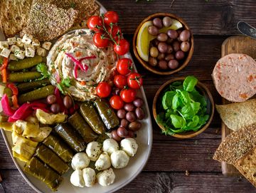 Mediterranean platter with hummus, olives, grape leaves, and fresh vegetables.