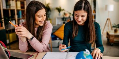 Two girls studying and smiling indoors.