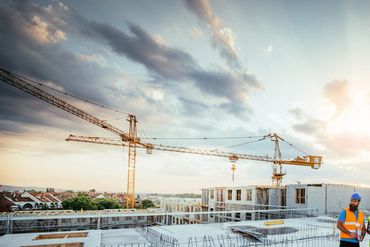 Three construction workers discuss plans on a building site at sunset.