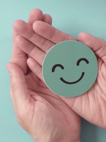 Hands holding a happy face symbol on a light blue background.