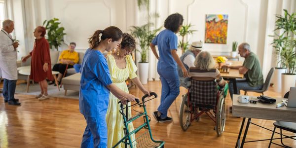 Nurse assisting elderly woman with walker in a lively care facility.