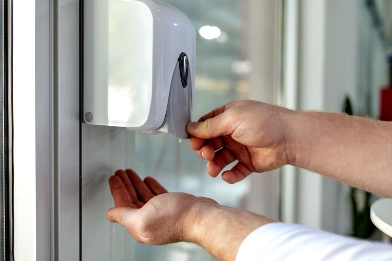 Man hand using wash hand sanitizer gel dispenser automatic machine for prevent Coronavirus. Male hands using automatic alcohol dispenser sanitation for cleaning hands, protection spread of bacteria.