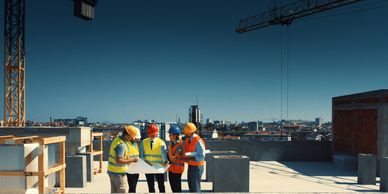 Construction workers reviewing plans on a rooftop under a clear sky.