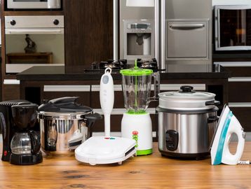 Various kitchen appliances arranged on a wooden table in a modern kitchen.