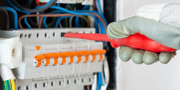 Electrician working on a circuit breaker panel with insulated tools and gloves.