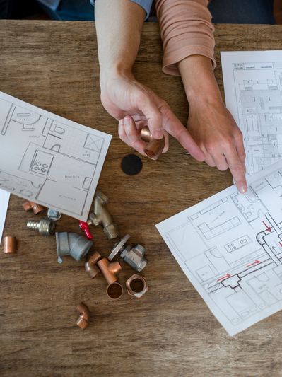 Two people reviewing architectural blueprints and plumbing parts on a wooden table.