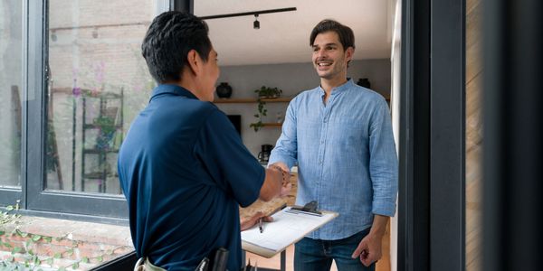 Two men shaking hands, one with tools and clipboard, inside a home.