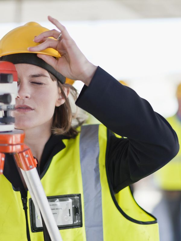 Female surveyor adjusting equipment on construction site wearing safety gear.