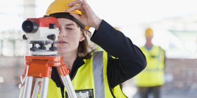 Female surveyor adjusting equipment on construction site wearing safety gear.