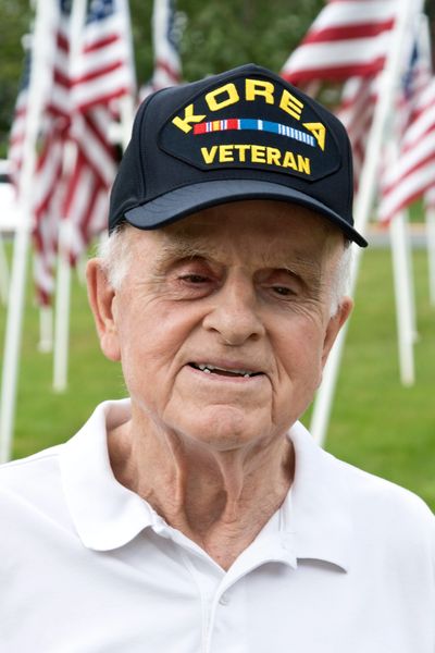 Elderly man wearing a Korea Veteran cap with American flags in the background.