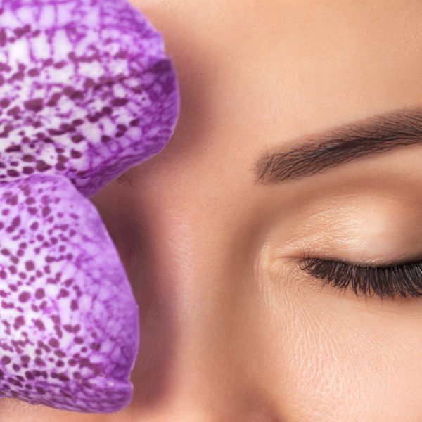 Close-up of a closed eye next to a vibrant purple orchid flower.