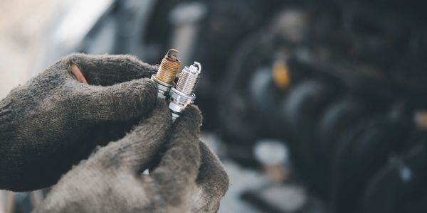A person holding two spark plugs. One old and one new.