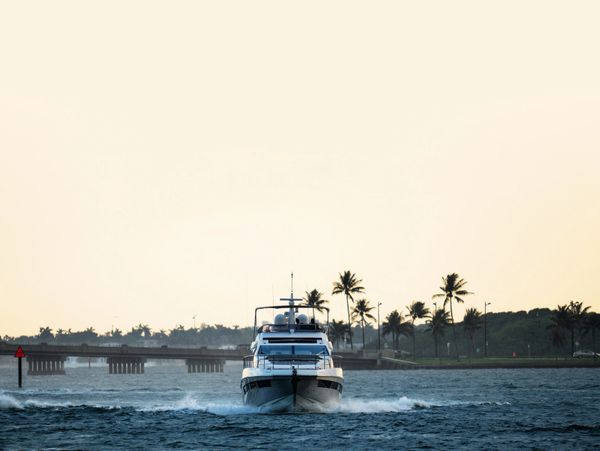 A yacht cruising towards the camera on a calm sea at sunset.