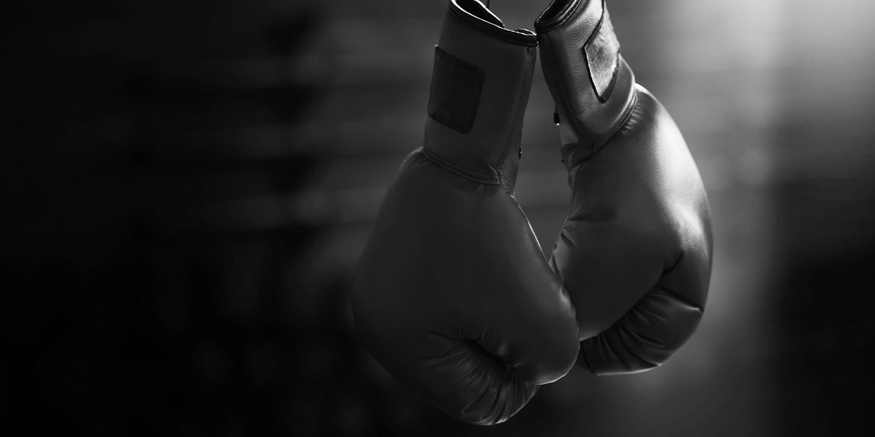 Red boxing gloves hanging against a dark background.
