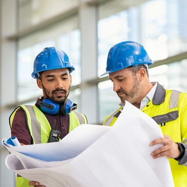 Construction supervisors reviewing blueprints inside a modern jobsite building, wearing safety helme