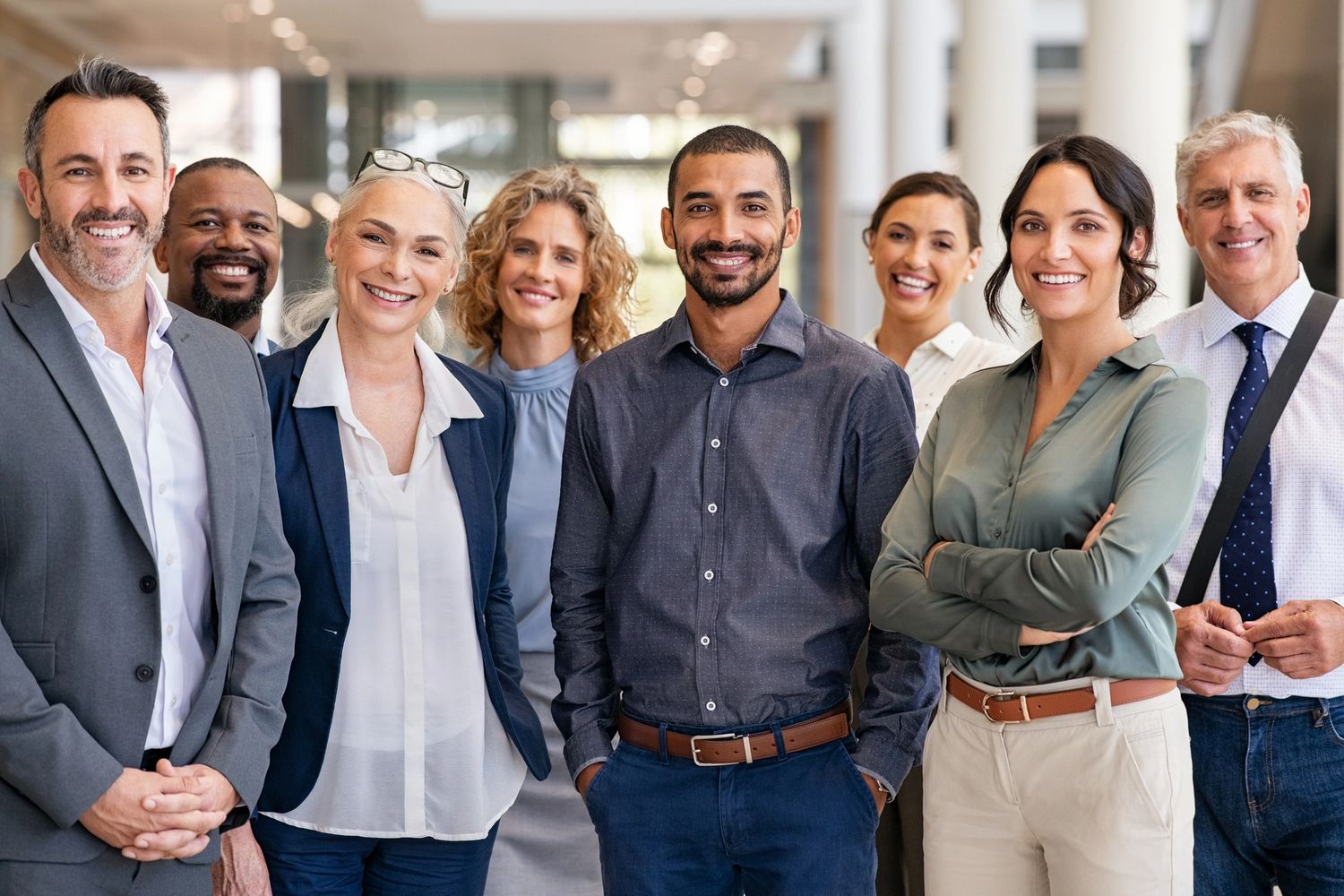 A diverse group of eight professionals smiling confidently indoors.