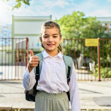 Smiling schoolgirl giving a thumbs up outdoors.
