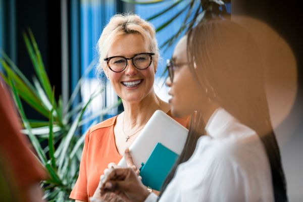 Two women engaged in a friendly conversation in a bright office.