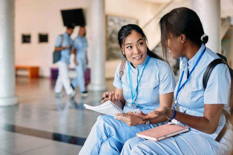 Multiracial medical students communicating while learning at university hallway. Focus is on Asian student.