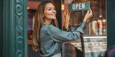 Smiling woman hanging an open sign on a shop door.