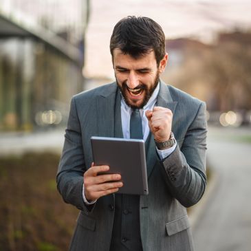 Man in suit excitedly using a tablet outdoors.