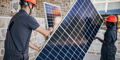 Two workers installing solar panels wearing orange safety helmets.