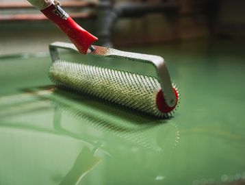 A spiked roller tool being used on a green liquid surface.