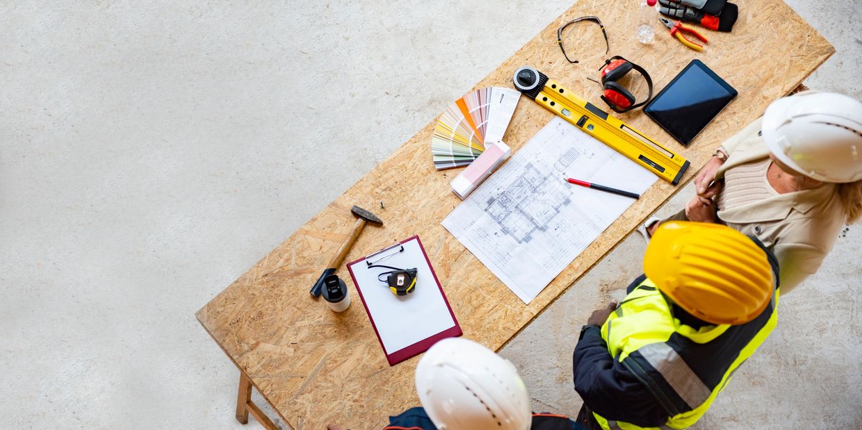 Construction workers reviewing blueprints and color samples on a wooden table.
