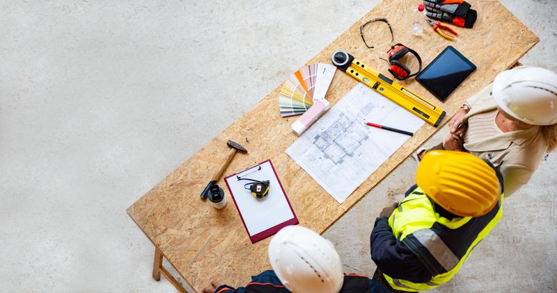 Team of one women architect and two men architects on a construction site. They are looking at blueprint. They are discussing about their project. Shot from above.