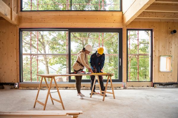 Two construction workers reviewing plans inside a wooden building under construction.