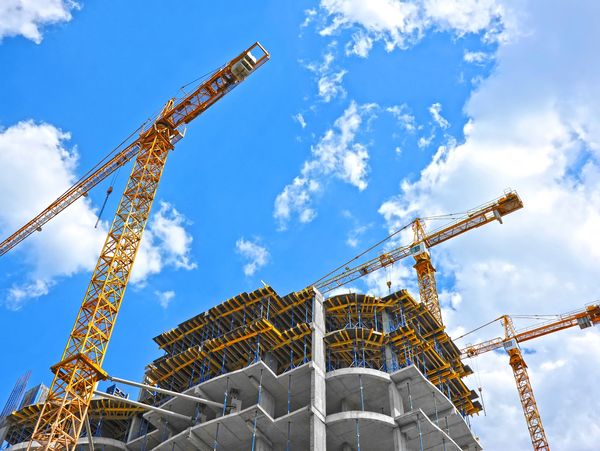 Construction cranes working on a modern building under a bright blue sky.