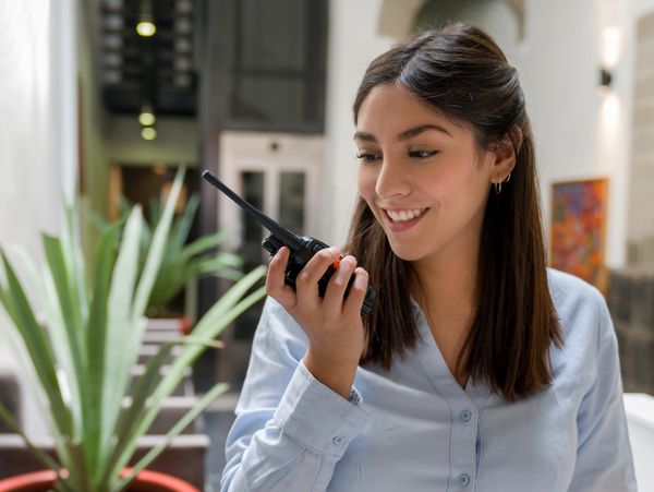 A smiling woman using a walkie-talkie indoors.