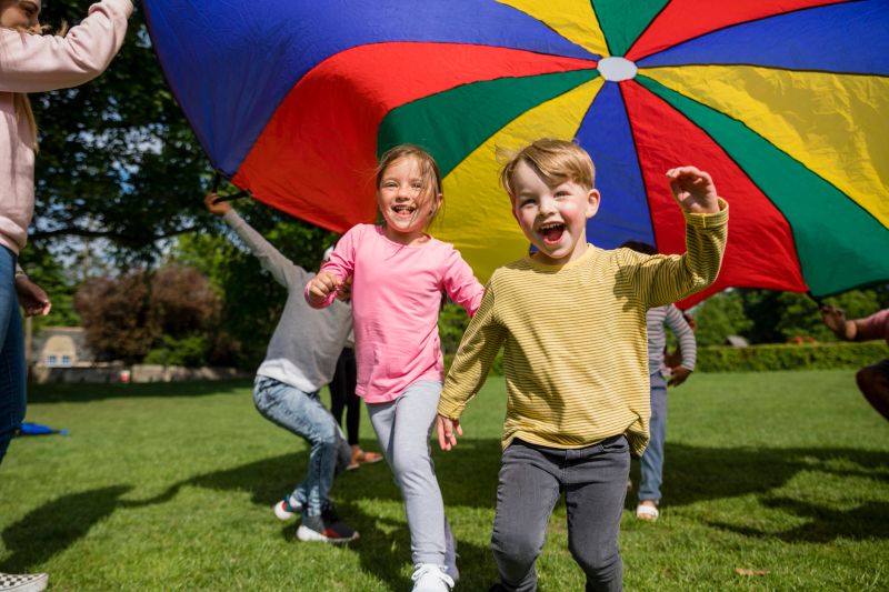 Children playing with a parachute at preschool in the North East of England. The children are running underneath it.