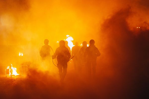 Silhouettes of people walking through fire and smoke.