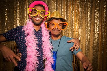 Two friends in oversized glasses and hats posing joyfully against a golden backdrop.