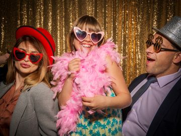 Three people in fun accessories posing happily against a gold sequin backdrop.