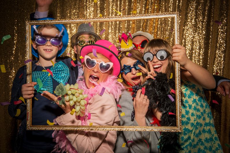 Portrait of cheerful male and female friends wearing party props and taking funny photo with picture frame during the party.