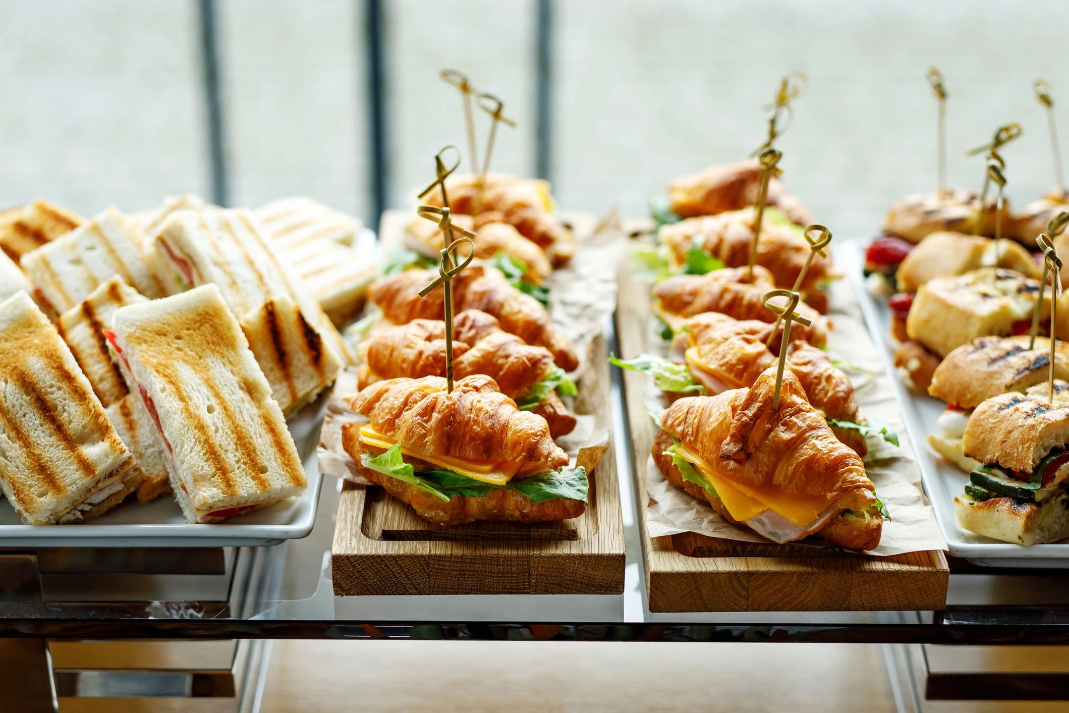 Assorted sandwiches and croissant sandwiches arranged on wooden and white trays.