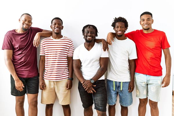 Five young men standing together smiling against a white background.